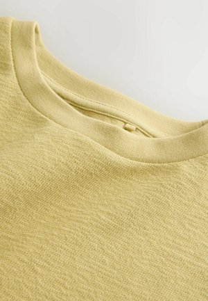 Világos sárga rövid ujjú póló texturált felülettel, bordázott kerek nyakkivágással és sima varrással a szélein.