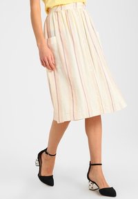 Gonna midi gialla chiara a righe con due tasche laterali, chiusura frontale con bottoni e vita arricciata. Abbinata a scarpe con tacco nere a punta con pois.