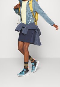 Blue patterned jacket, yellow backpack, light shirt, navy skirt, athletic shoes with blue and pink accents, and striped brown socks.