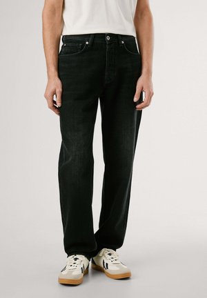 Jeans de mezclilla negra con corte recto, que cuentan con cinco bolsillos y un cierre de botón sencillo. Llevado con zapatillas de color claro.