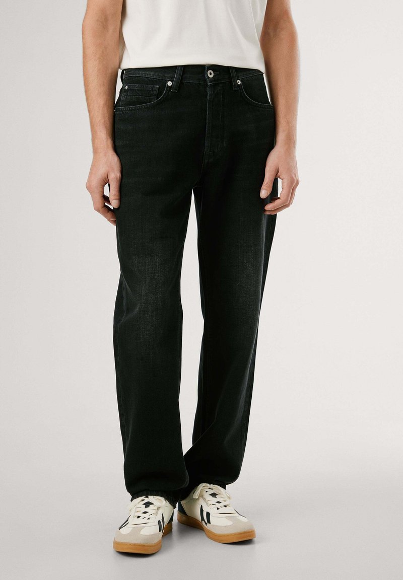 Mustast denimist valmistatud sirge lõikega teksad, viie taskuga disain ja hõbedane riistvara. Kombineeritud valgete tossudega, millel on tumesinised aktsendid.