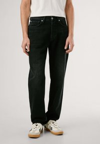 Jeans de mezclilla negra con corte recto, que cuentan con cinco bolsillos y un cierre de botón sencillo. Llevado con zapatillas de color claro.