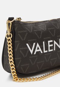 Svart läderhandväska med guldkedjeslits, dragkedjestängning och ett mönster som upprepas med "Valentino"-logotyp. Vit "VALENTINO"-tryck framträdande.