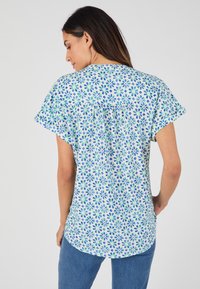Blusa de manga corta en azul claro con un estampado floral en verde y azul oscuro. Presenta un corte relajado y dobladillo redondeado.