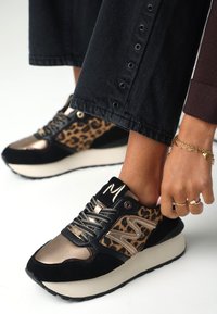 Svart och leopardmönstrad sneakers med metalliska guldaccenter, texturerad mocka och läder, tjock gräddfärgad sula och sydda detaljer på sidan.