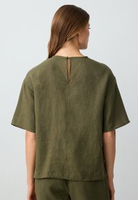 Top corto a maniche corte verde oliva con vestibilità rilassata, dotato di un'apertura a chiave sulla schiena sicura con un bottone e un tessuto morbido e strutturato.
