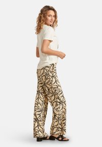 Witte T-shirt met korte mouwen, gecombineerd met losse, lichtbeige broeken met een zwart bloemenpatroon, gedragen met zwarte blokhak sandalen.