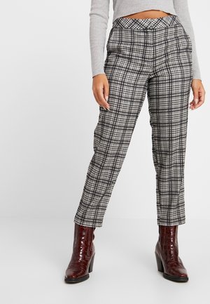 Woman wearing gray plaid pants, gray long-sleeve cropped top, and brown heeled ankle boots, standing against a light background.