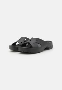 Sandales en plastique noir avec un bout ouvert, des bandes croisées présentant des trous de ventilation, un pied-texturé et une semelle basse et contournée.