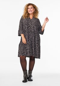 Robe à imprimé léopard avec un décolleté en V, des manches trois-quarts et une jupe à volants, associée à des bottines noires et des collants transparents.