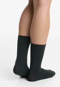 Gambe che indossano calze a coste nere, in piedi con un piede leggermente sollevato su uno sfondo bianco.