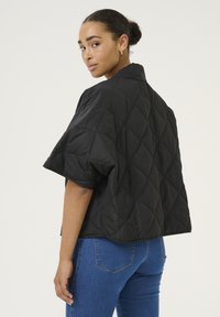 Sorte quiltede jakke med et cropped design, korte ærmer og en glat tekstur, parret med blå jeans og minimale detaljer.