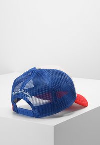 Gorra de malla azul con visera roja y panel frontal blanco. Cuenta con "Queridos Eco Machines" bordado en la parte trasera y cierre ajustable a presión.