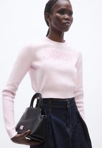 Maglione rosa chiaro con logo "tommy jeans" in rilievo, abbinato a una gonna in denim scuro. Borsa nera con design strutturato e manici corti.