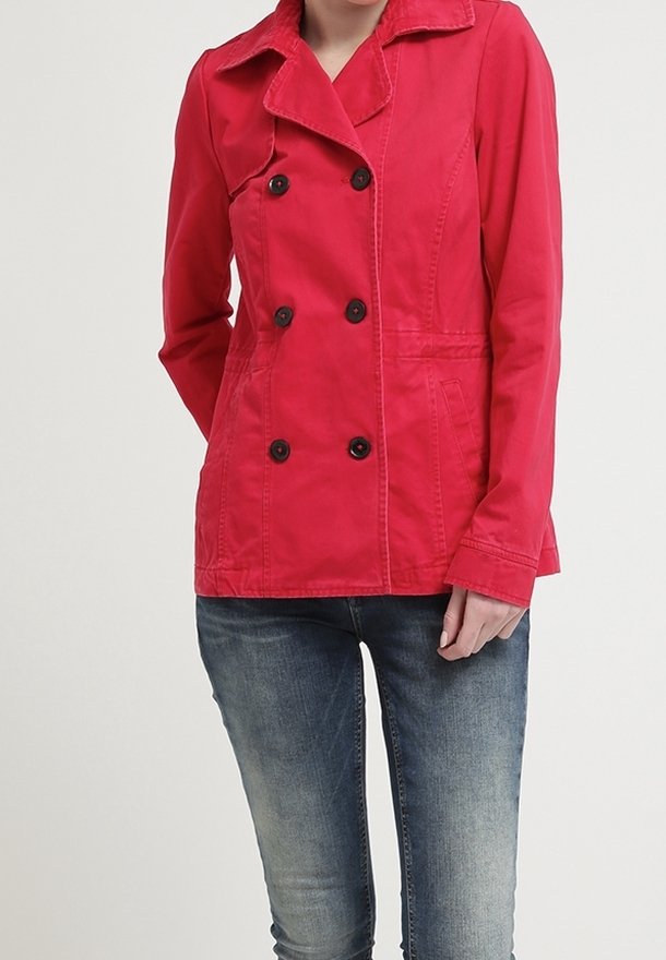 Abrigo corto rojo con diseño de doble botonadura, botones negros y cuello texturizado, combinado con vaqueros azules. La tela parece suave y ligera.