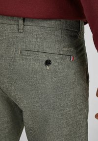 Grijze geruite broek met een knoopsluiting, zijzakken en een achterzak met een zwarte knop. Logo in lichte borduursel op de tailleband.