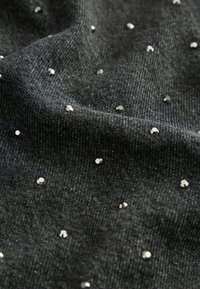 Tessuto nero testurizzato con una leggera lucentezza, caratterizzato da decorazioni metalliche sparse che creano un motivo a pois sulla superficie.