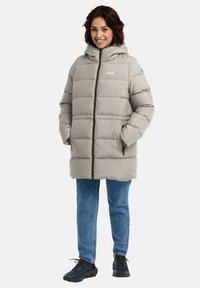 Lichtgrijze pufferjack met een capuchon, voorzien van een ritssluiting aan de voorkant, zijzakken en een gestikt patroon. Gecombineerd met blauwe jeans en zwarte schoenen.