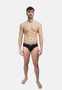 Slip di cotone nero con elastico morbido in vita recante il logo "Liu Jo", caratterizzati da una vestibilità aderente e un design minimalista, modello in piedi a piedi nudi.