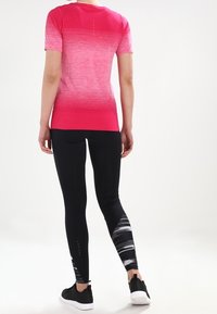 Lyhythihainen rosa-gradienttipaita, joka on yhdistetty mustiin legginsseihin, joissa on abstrakteja harmaita kuvioita. Pyöreä pääntie ja sileä kankaan rakenne.