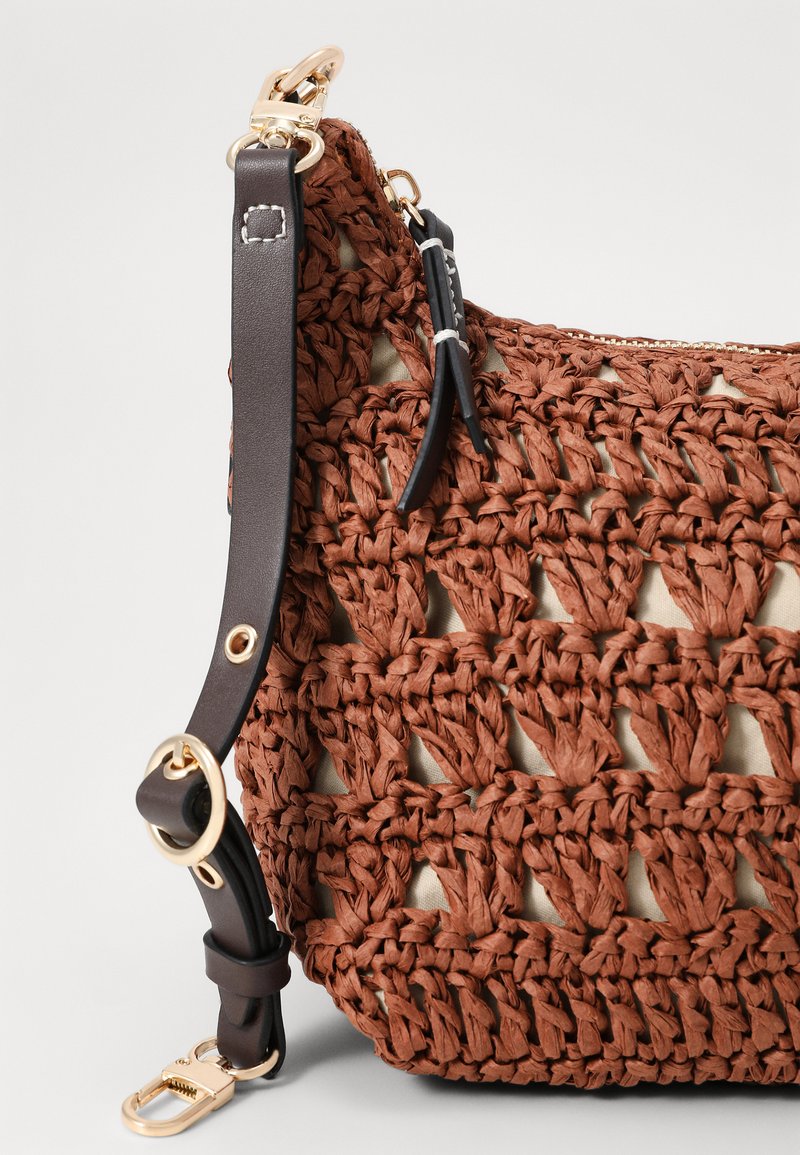Bolso tejido marrón con un diseño de croché texturizado, interior beige y una correa de cuero oscuro con acentos de herrajes en tono dorado.