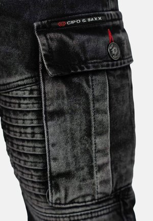Black denim cargo pants with textured ribbing on sides, a flap pocket, and a logo tag. Features silver hardware and a fitted design.
