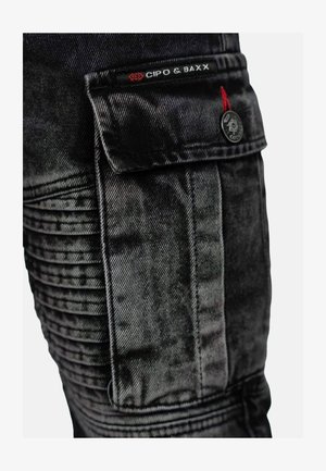 Pantalons cargo en denim noir avec un galon texturé sur les côtés, une poche à rabat et une étiquette de logo. Présente des éléments en métal argenté et une coupe ajustée.
