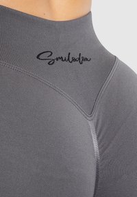 Graues Sportoberteil mit hohem Kragen, eng anliegendem Design, glatter Textur und kontrastierendem, gesticktem Markennamen.