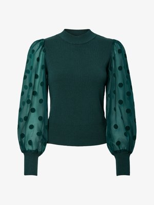Zaļa rievojuma džemperis ar augstu apkakli un caurspīdīgām pūkainām piedurknēm, kas dekorētas ar melniem punktiņiem. Pieguļošs apakšmala un piedurknes noslēdz dizainu.