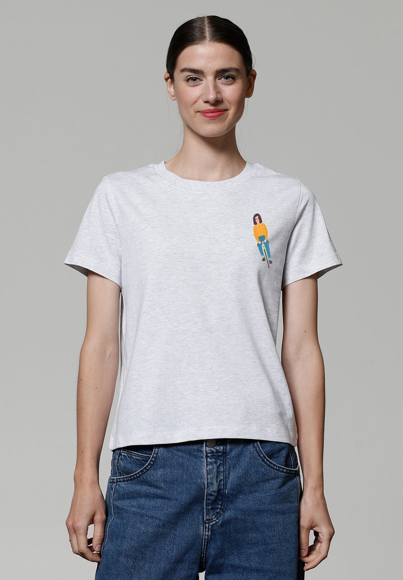 T-shirt en coton gris clair à manches courtes ; présente un graphique coloré d'une personne portant un haut orange et un jean bleu sur la poitrine gauche.