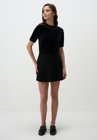 Czarny puszysty top z krótkim rękawem, z wykończeniem w ćwieki, połączony z czarną plisowaną mini spódnicą w wysokim stanie. Uzupełniony czarnymi mokasynami.