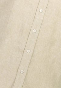 Cămașă din in khaki, cu un nasture la gât, șase nasturi mici albi și un material texturat, țesut.