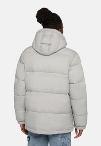 Jasnoszara kurtka puchowa z kapturem, posiadająca pikowane sekcje i elastyczne mankiety. Tkanina wydaje się gładka i wodoodporna.