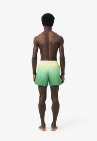 Costumi da bagno verde ombre con una cintura gialla. Il materiale è un tessuto leggero, dotato di una tasca posteriore e una cintura elastica.