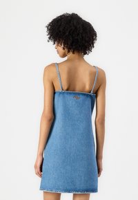 Denimmekko keskipunaisena, ohuiden olkaimien, löysän istuvuuden ja repsottavan helman kanssa. Sisältää huomaamatonta tikkausta ja pienen logoyksityiskohdan takana.