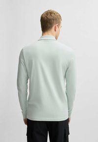 Vaaleanvihreä pitkähihainen polo-paita, sileä pinta, klassinen kaulus, suora helma, yhdistetty mustiin cargo-housuihin, yksinkertainen takanäkymä.