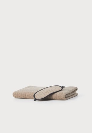 Mjuk beige ullfilt med ett strukturerat stickat mönster, vikt tillsammans med en matchande sovmask med en mörk kant.