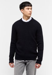 Granatowy sweter dzianinowy z okrągłym dekoltem, ściągaczami przy rękawach i na dole, z teksturowanym wzorem i metką logo w lewym dolnym rogu.