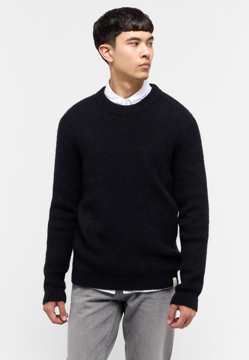 Granatowy sweter dzianinowy z okrągłym dekoltem, ściągaczami przy rękawach i na dole, z teksturowanym wzorem i metką logo w lewym dolnym rogu.
