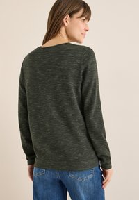 Oliwkowo-zielony sweter z teksturowanym splotem, okrągłym dekoltem i długimi rękawami, zestawiony z niebieskimi dżinsami.