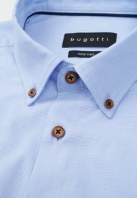 Hellblaues, strukturiertes Button-Up-Hemd mit gesteiftem Kragen, braunen Knöpfen und "Bugatti Easy Care"-Etikett.