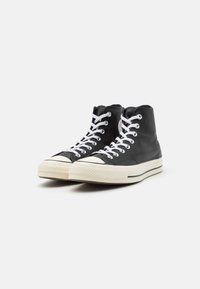 Sneaker alte in pelle nera con lacci bianchi e suola in gomma. Presentano una punta rotonda e un cappuccio in gomma testurizzata. Elementi di design classici.