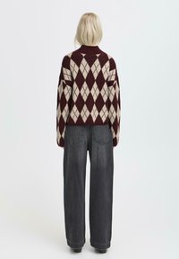 Maglione argyle bordeaux e crema lavorato a maglia con collo alto; vestibilità ampia e maniche larghe, abbinato a jeans a gamba larga grigi scuri a vita alta.