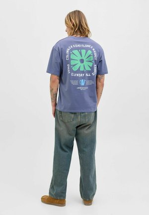T-shirt en coton lavande à manches courtes avec un graphisme floral vert et du texte au dos. À associer avec un jean baggy, bleu clair et taille haute.