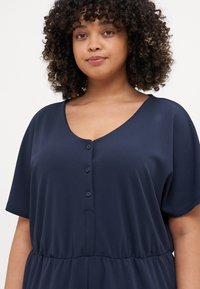 Navy blue dress made of soft fabric, featuring a V-neck, short sleeves, and a button-front closure with an elastic waist for a relaxed fit.