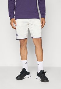 Valged sportlikud lühikesed püksid purpursete ääristega, millel on Adidas'i logo; kombineeritud mustade tossudega ja valgete sokkidega, millel on logo. Peal on purpurne dressipluus.
