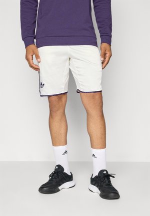 White athletic shorts with purple trim, featuring an Adidas logo; paired with black sneakers and white socks with logo. Purple sweatshirt on top.
