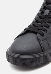 Zapatillas de cuero negro con punta redondeada, suela texturizada, cordones negros planos y un diseño minimalista con sutiles detalles de costura.