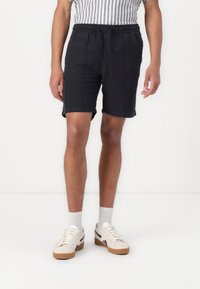 Zwarte shorts met een elastische tailleband, vallend tot halverwege de bovenbenen, gecombineerd met witte sneakers en lichte sokken, met een gladde stoftextuur.