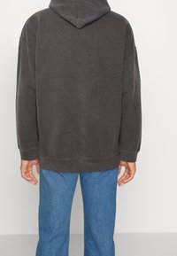 Felpa oversize grigia scura con cappuccio regolabile, polsini e fondo a costine. Abbinata a jeans blu a gamba dritta. Tessuto morbido e testurizzato.